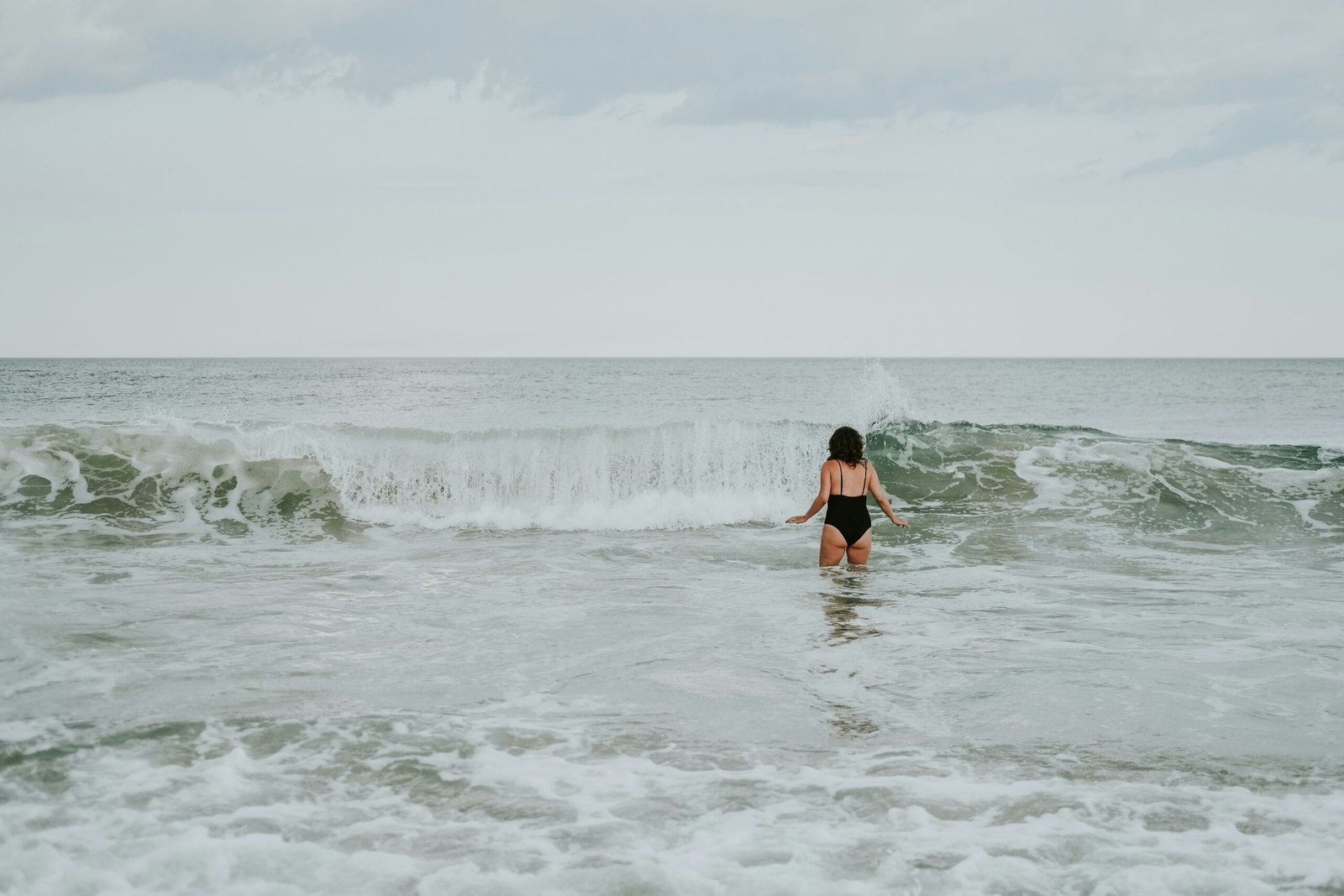 woman in black bikini walking on sea waves during daytime